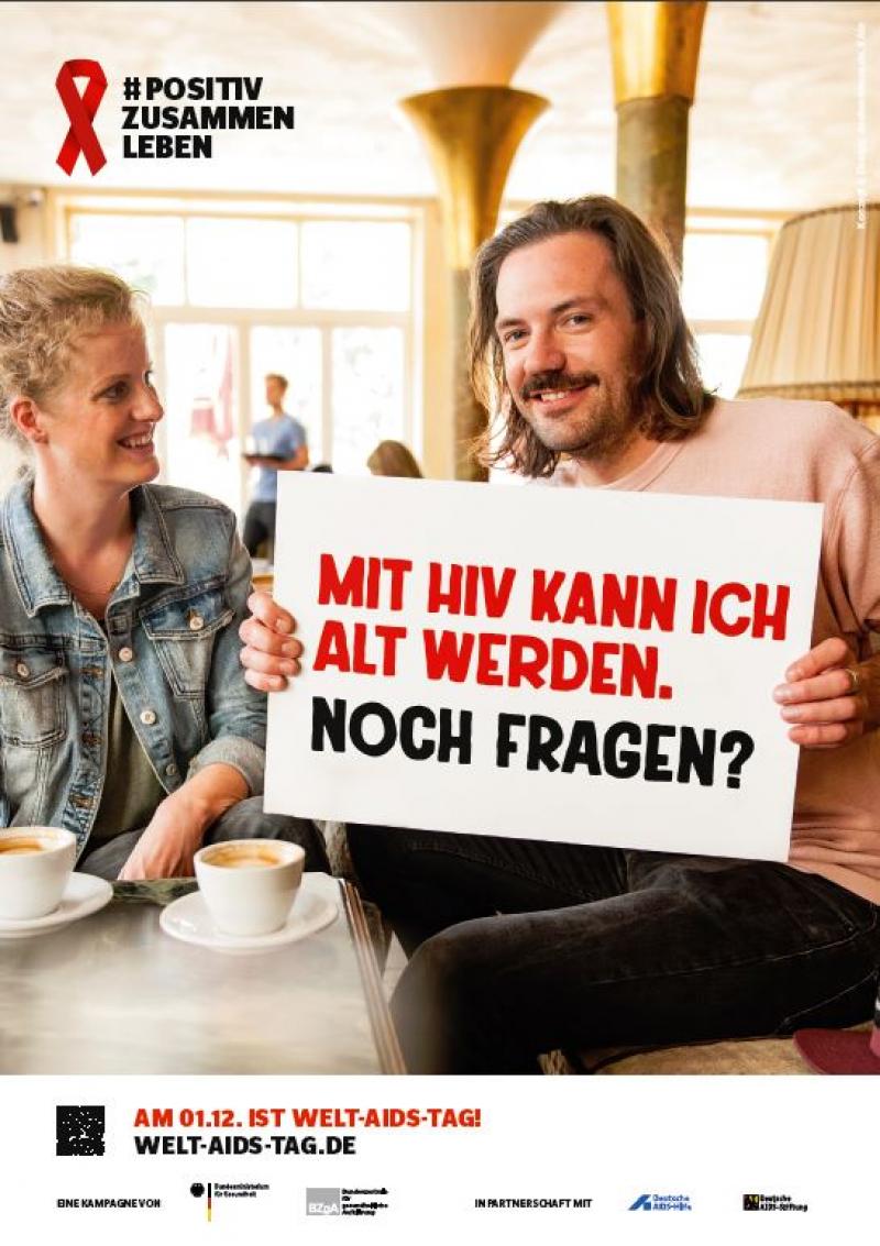 Mann mit Schild in der Hand. Neben ihm eine Frau. Text auf dem Schild: "Mit HIV kann ich alt werden. Noch Fragen?