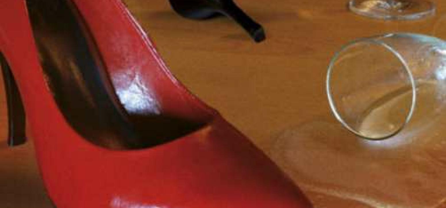 Roter Stöckelschuh, umgekipptes Sektglas, Kondomverpackung auf Holzfußboden