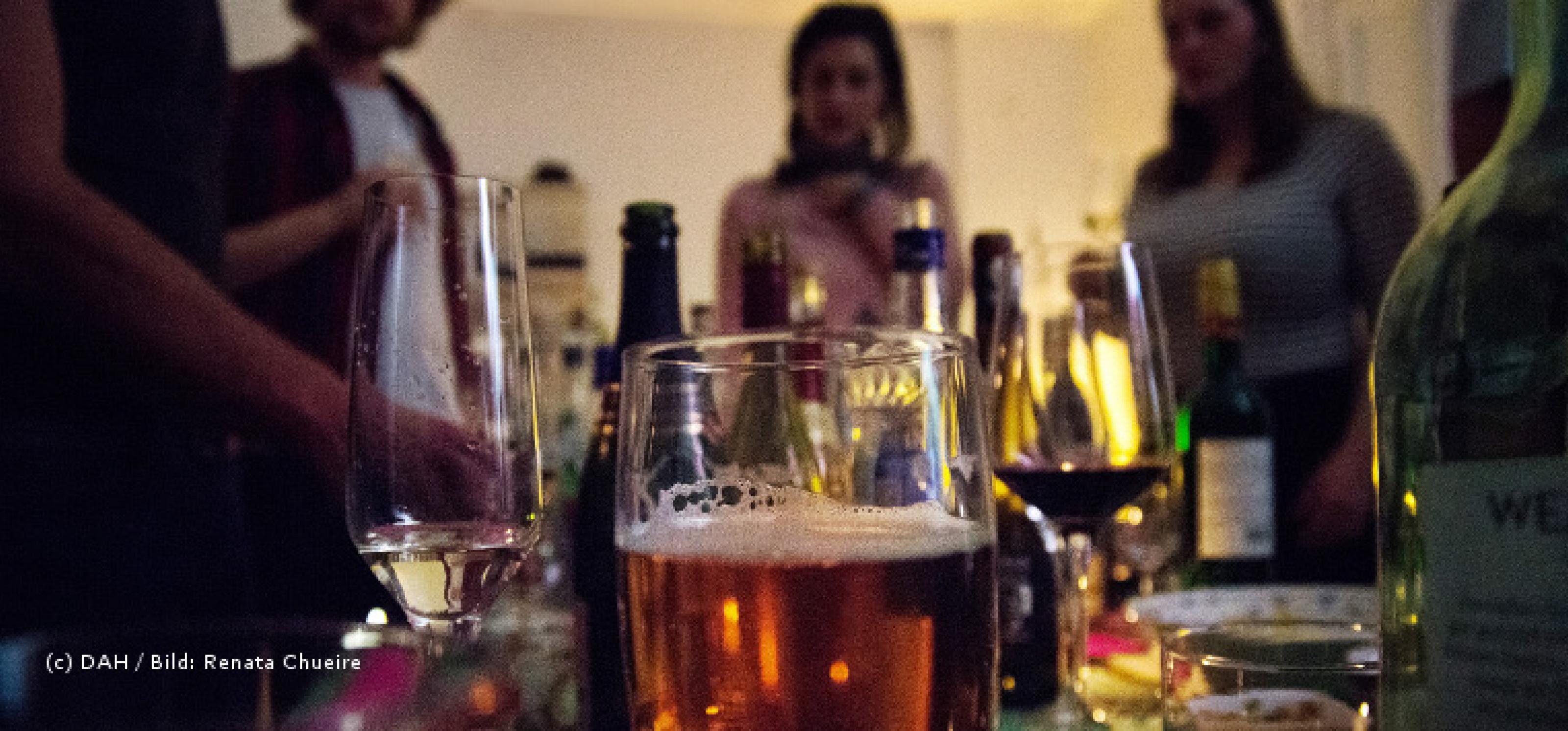 Blick auf eine Partyszene, im Vodergrund stehen mehrere alkoholische Getränke, im Hintergrund die Silhouetten von einigen Menschen