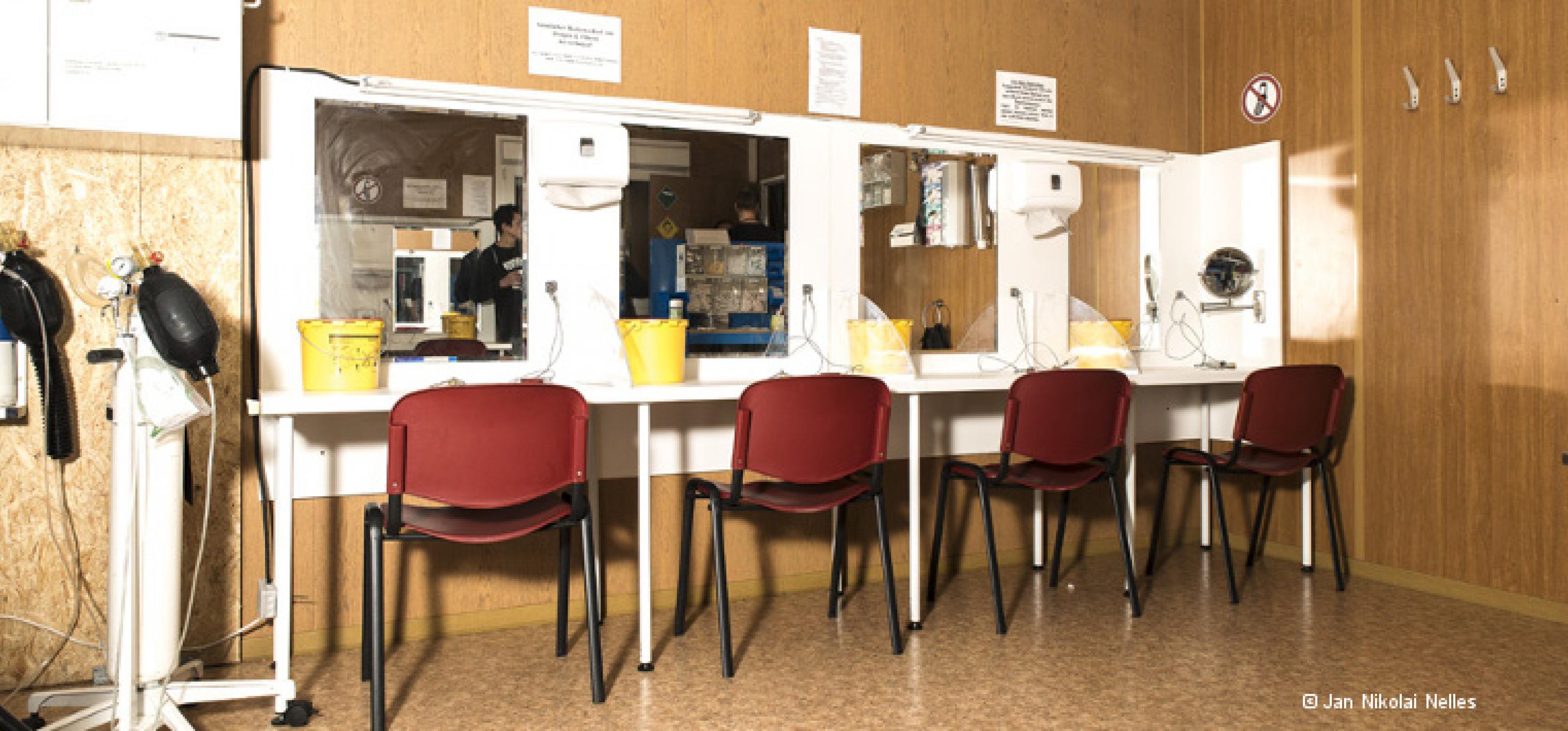 Drogenkonsumraum: Entlang einer Wand stehen vier Stühle vor Tischen und Spiegeln, an denen Drogen gespritzt werden können. An der Seite stehen zwei Beatmungsgeräte.