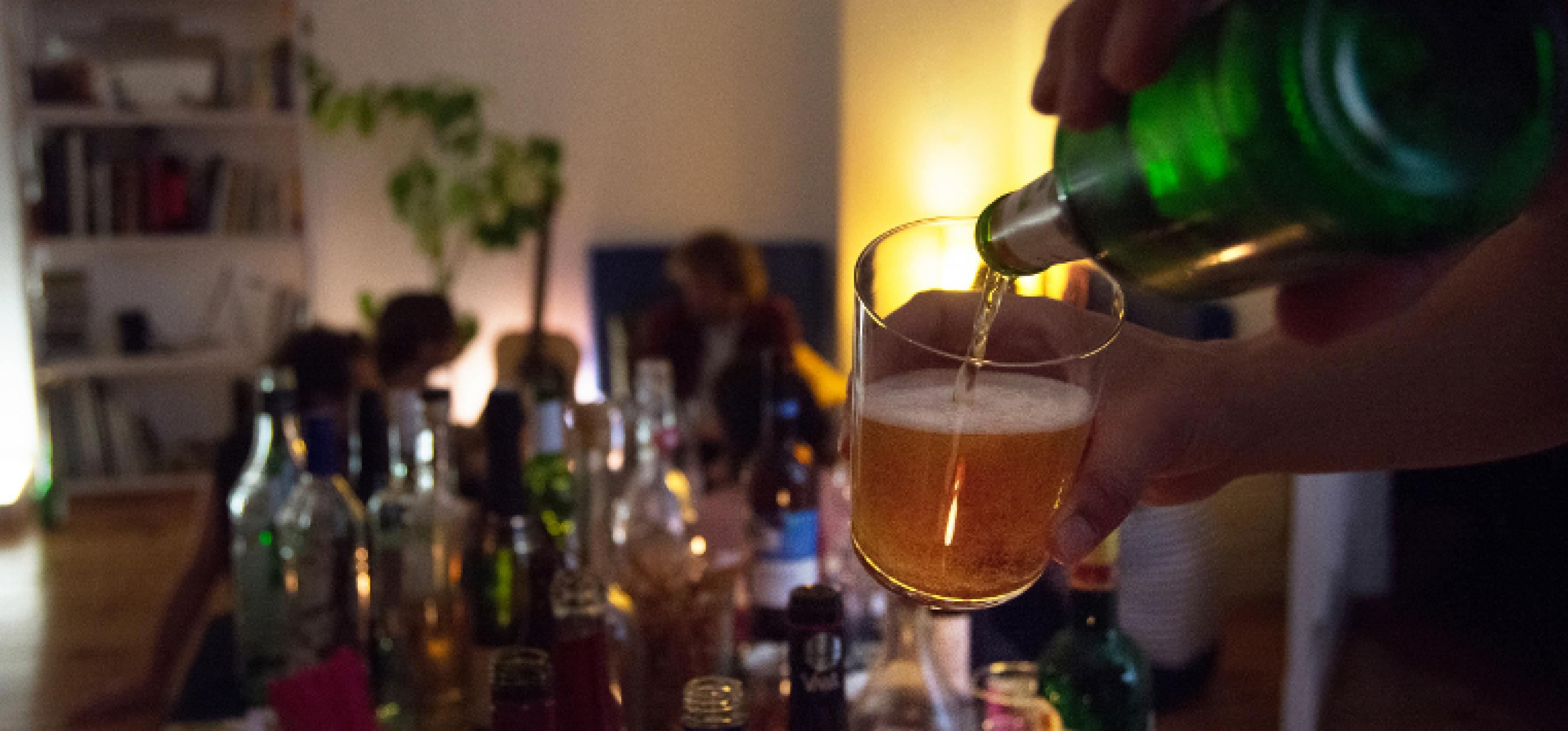 Eine Partyszene im Dämmerlicht, auf einem Tisch stehen verschiedene Gläser und Flaschen mit Alkohol
