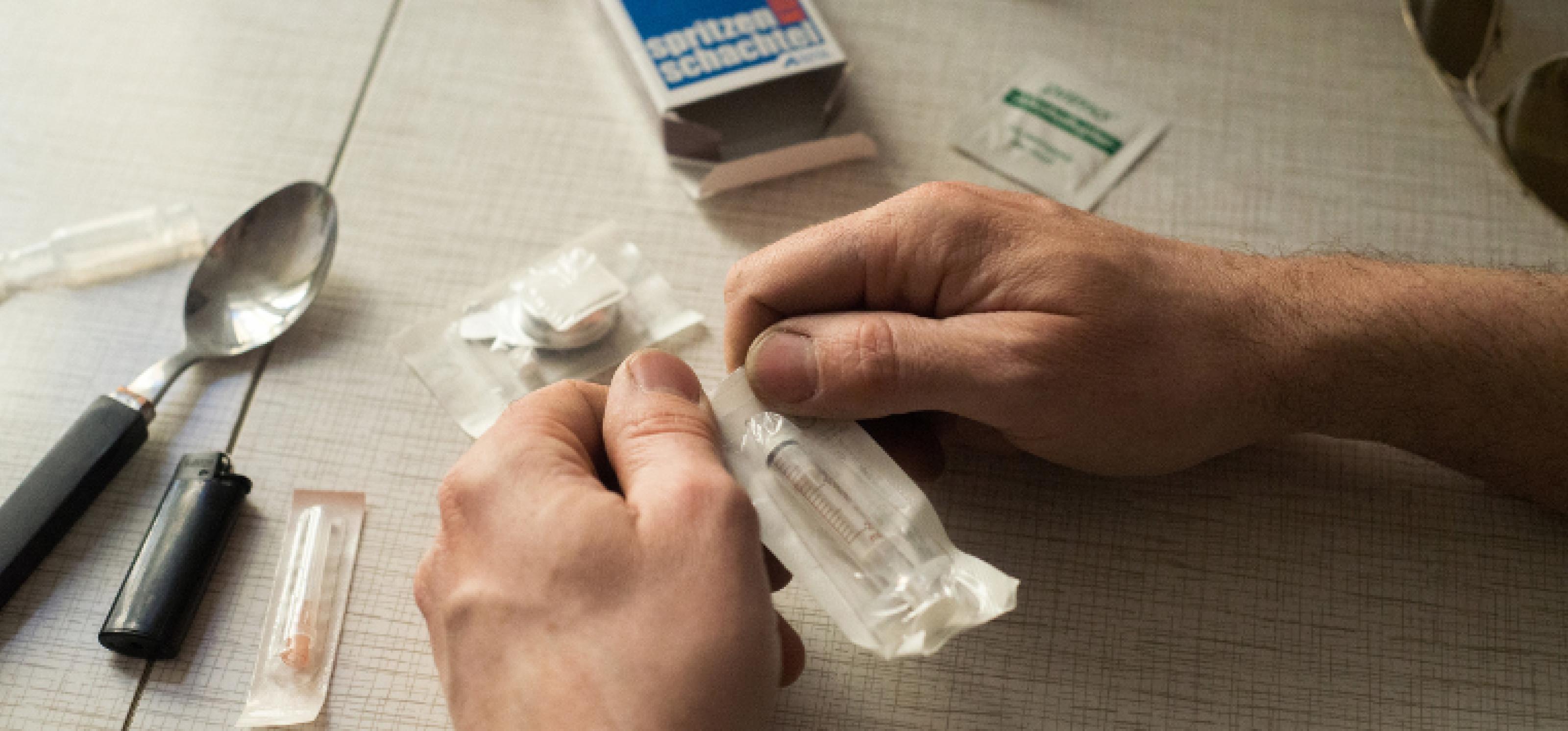 Zwei Hände öffnen die Verpackung einer steril eingepackten Spritze für Safer Use